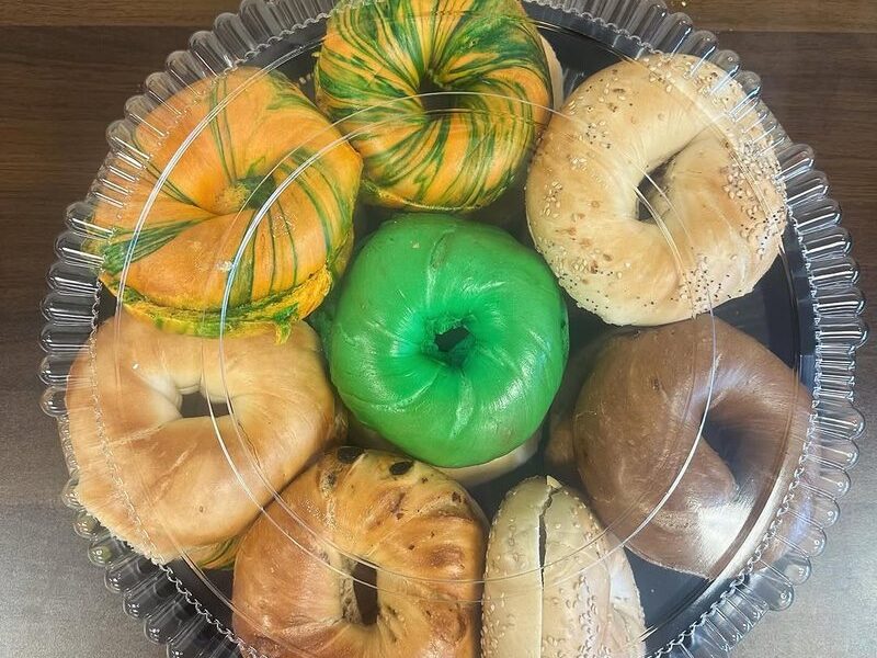 A box of assorted bagels including a green bagel and rainbow swirl bagels