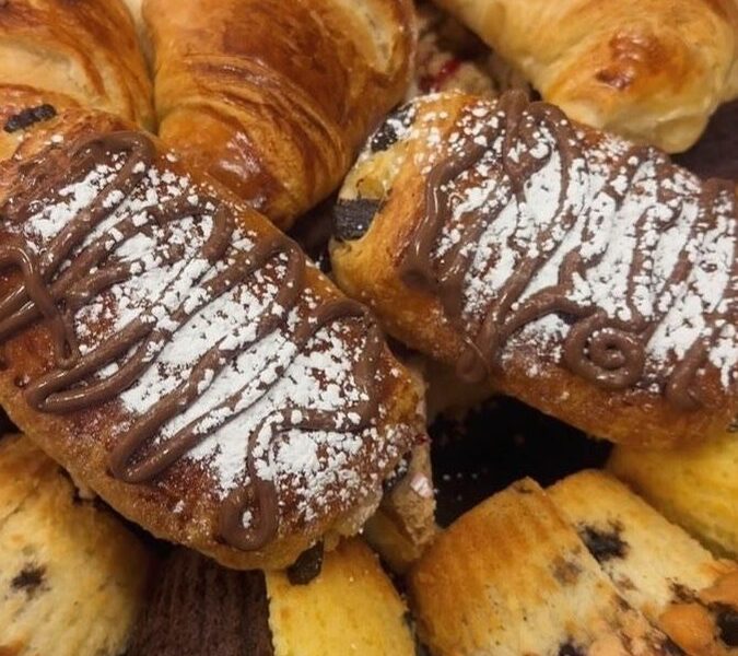 A tray of croissants, chocolate-drizzled pastries and muffins